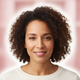 Portrait of a smiling woman with a soft, genuine expression, looking at the camera. The background is blurred in shades of pi
